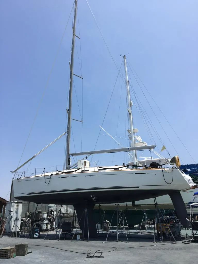 Slide: The Image of 2005 Beneteau First 44.7 sailboat on dry dock, showcasing sleek design and tall mast. - 2