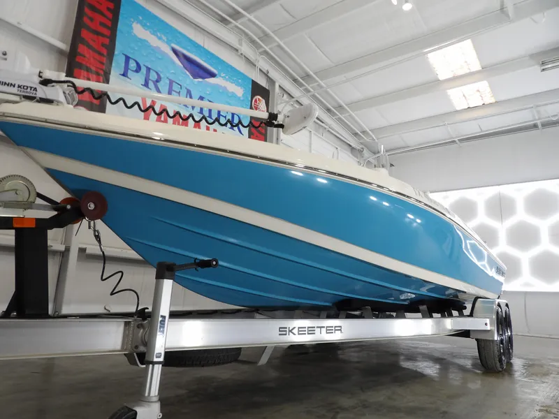 Slide: The Image of 2019 Skeeter SX210 boat in showroom, blue hull on trailer, indoor lighting. - 5
