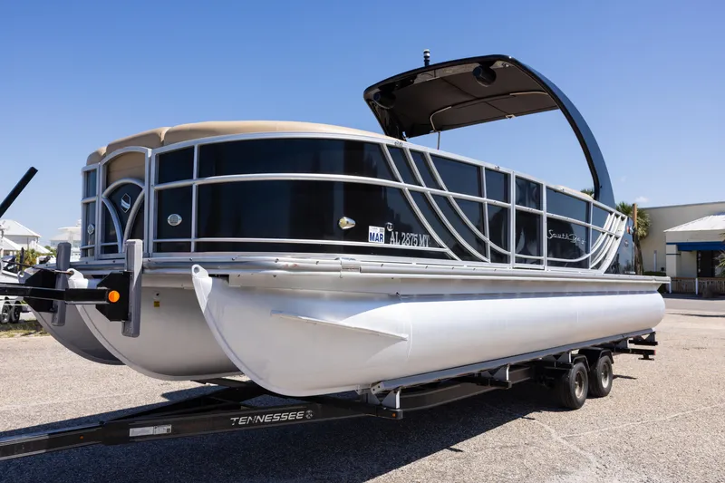 Slide: The Image of 2015 South Bay 724 SPORT DLX pontoon boat on a trailer, parked outdoors. - 2