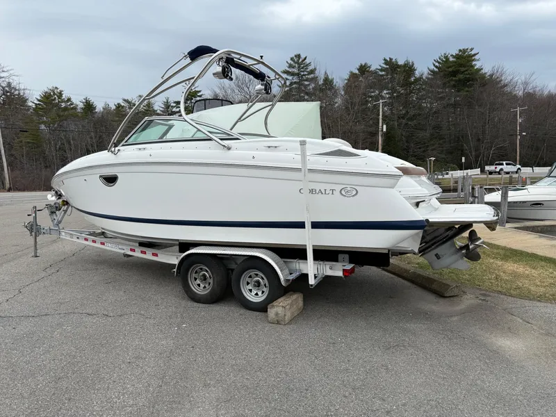 Slide: The Image of 2013 Cobalt 242 boat on trailer, parked outdoors, with overcast sky and trees in background. - 3