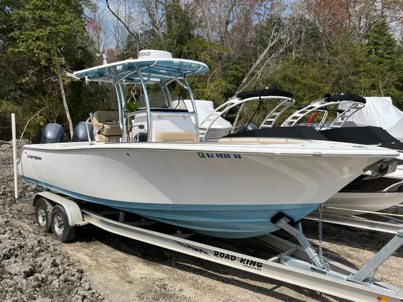 Slide: The Image of 2017 Sportsman 252 boat on trailer, parked outdoors, surrounded by trees and other boats. - 0