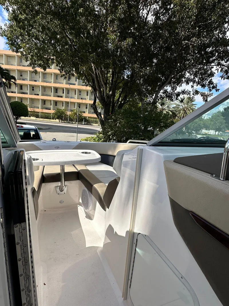 Slide: The Image of 2013 Regal 24 FasDeck boat interior with seating and table, parked near trees and building. - 3