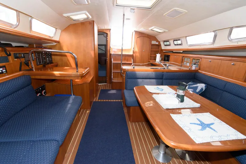 Slide: The Image of 2004 Hunter 44 Deck Salon interior with blue seating, wooden finishes, and dining area. - 16