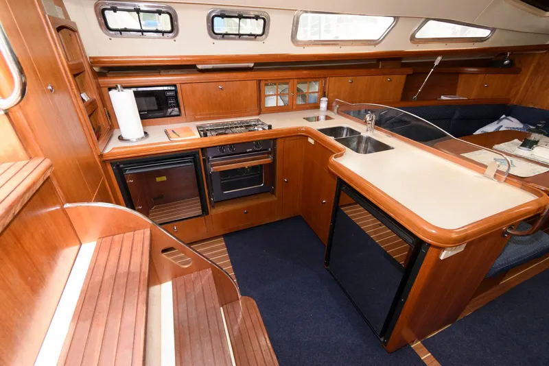 Slide: The Image of 2004 Hunter 44 Deck Salon interior with wood cabinetry, kitchen appliances, and seating area. - 17