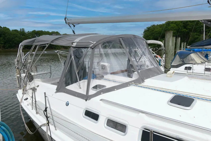 Slide: The Image of 2004 Hunter 44 Deck Salon sailboat docked, featuring a sleek design and protective canopy. - 2