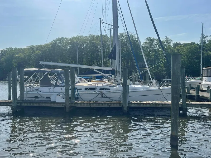 Slide: The Image of 2004 Hunter 44 Deck Salon sailboat docked at a marina, surrounded by trees. - 3
