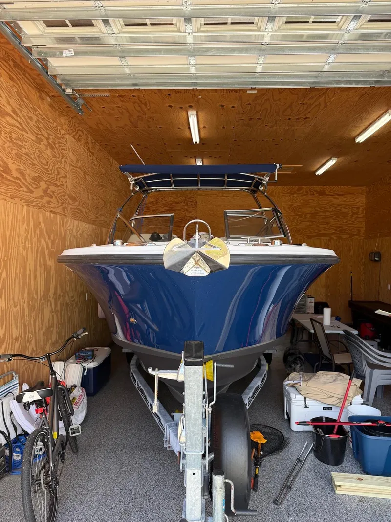 Slide: The Image of 2012 Edgewater 245 CX boat in garage, blue hull, trailer, storage items nearby. - 1