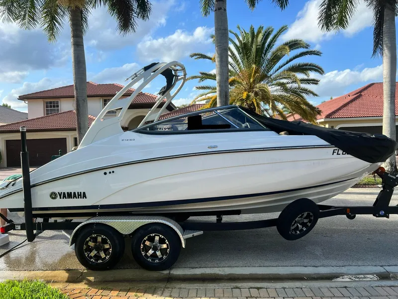 Slide: The Image of 2022 Yamaha Boats 212SD on trailer, parked near palm trees and houses. - 2