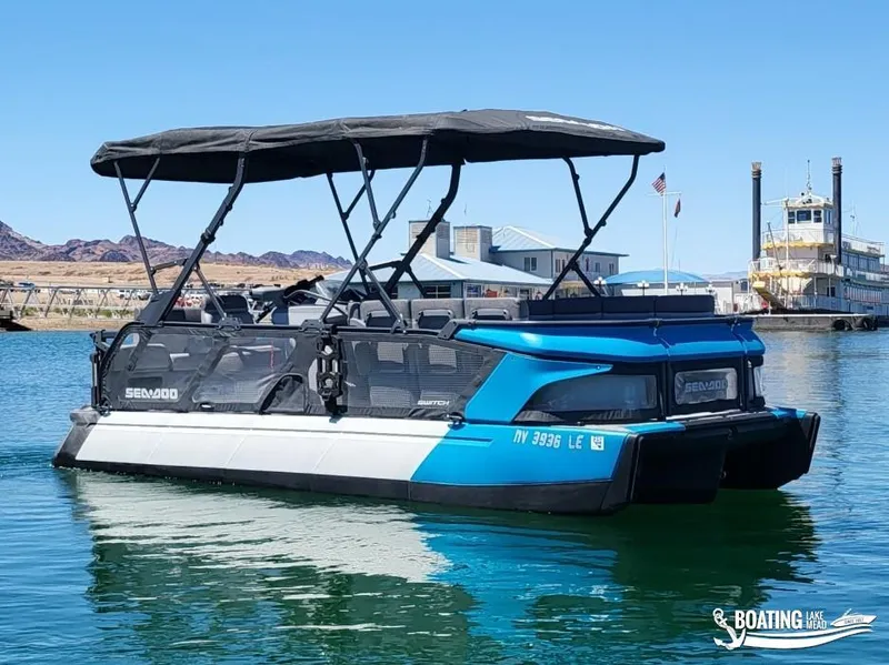 Slide: The Image of 2023 Sea-Doo Switch Cruise 21 pontoon boat on calm water near a dock. - 2
