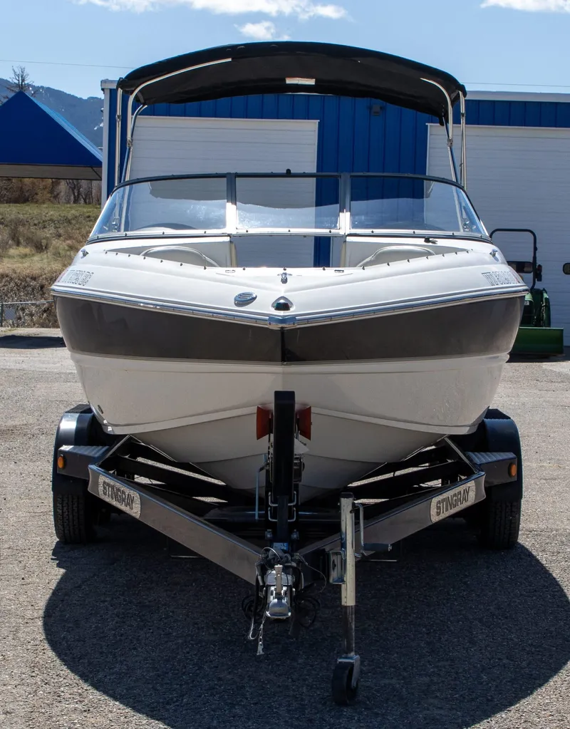 Slide: The Image of 2013 Stingray 225 LR boat on trailer, front view, parked outdoors. - 2