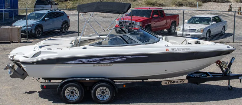 Slide: The Image of 2013 Stingray 225 LR boat on trailer, parked near cars in a lot. - 3