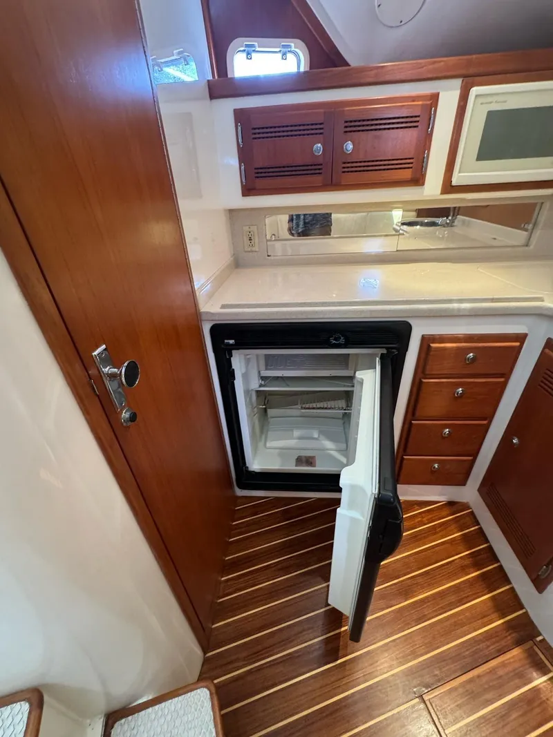Slide: The Image of 1998 Cabo 35 Express yacht interior with open fridge, wooden cabinets, and striped flooring. - 22