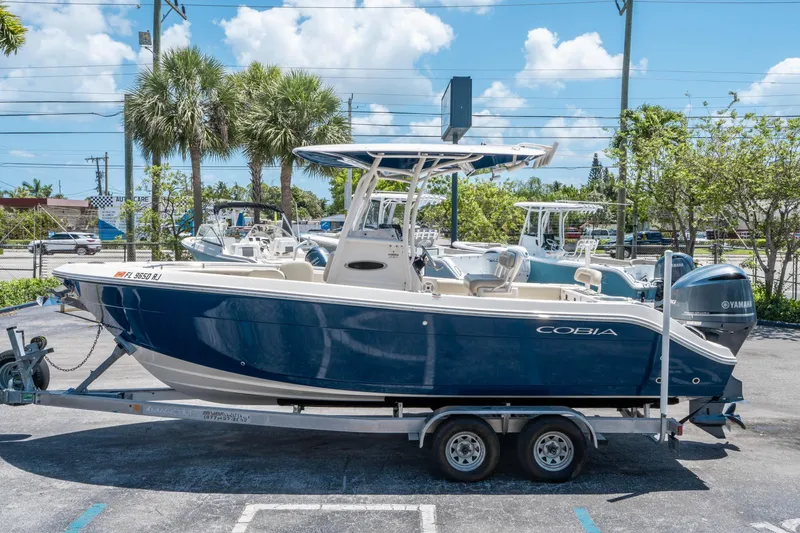 Slide: The Image of 2017 Cobia 237 CC boat on trailer, parked outdoors under a clear blue sky. - 5