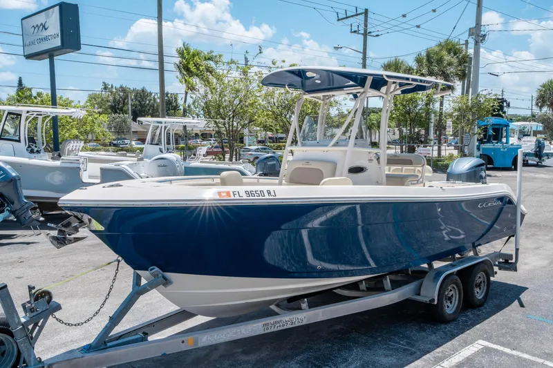 Slide: The Image of 2017 Cobia 237 CC boat on trailer at dealership under clear blue sky. - 6