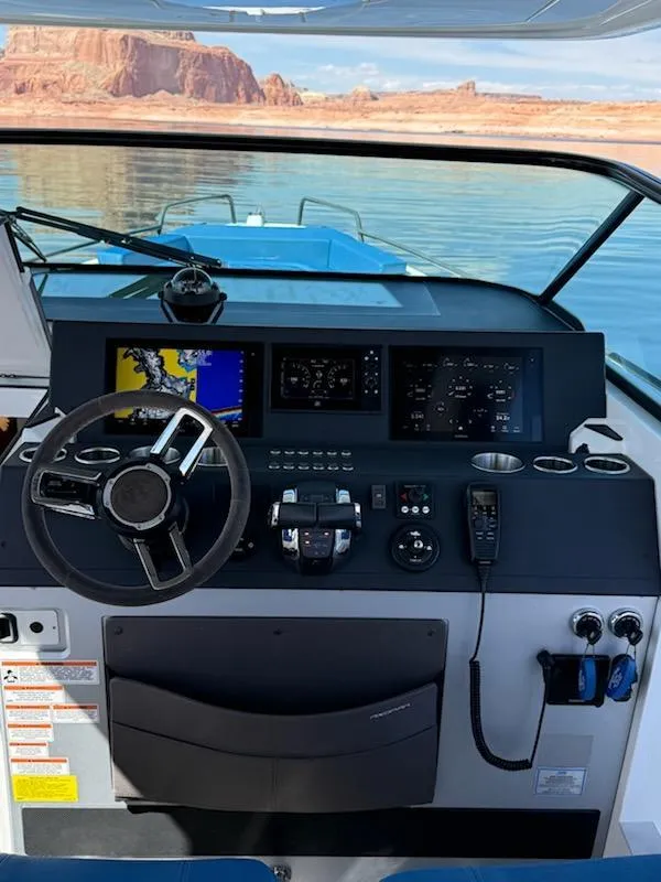 Slide: The Image of 2019 Axopar Brabus boat dashboard with navigation screens, steering wheel, and scenic water view. - 2