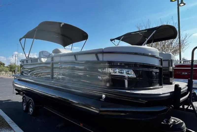 The Image of 2024 Regency 250 LE3 pontoon boat with dual bimini tops, parked on a trailer. - 0