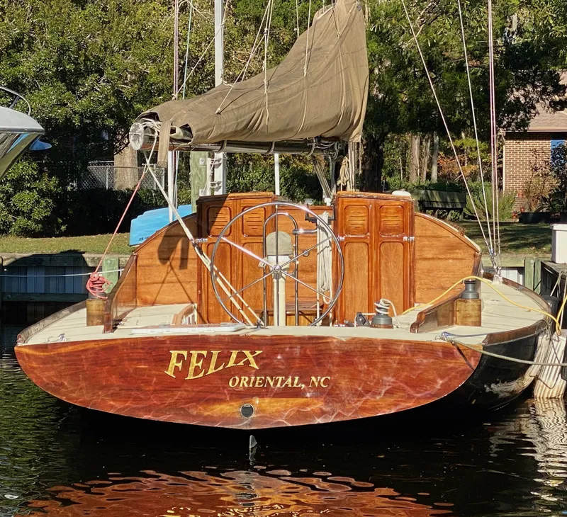 Slide: The Image of 37ft custom catboat yacht docked, featuring wooden finish and covered sail, named "Felix" from Oriental, NC. - 3