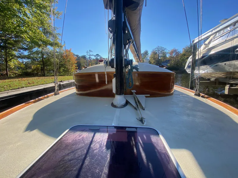 Slide: The Image of 37ft Catboat Yacht on calm water, showcasing deck and mast, surrounded by trees and clear sky. - 34