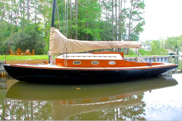Slide: The Image of 37ft custom catboat yacht with wooden cabin, docked on calm water, surrounded by trees. - 6