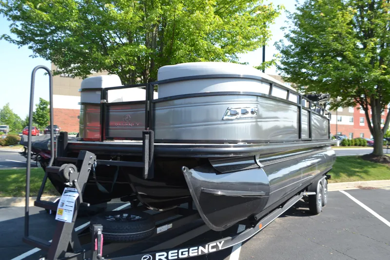 Slide: The Image of 2025 Regency 250 DL3 pontoon boat on trailer, parked outdoors with trees in background. - 1