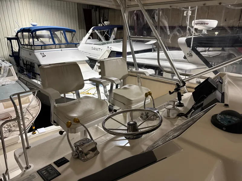 Slide: The Image of 1990 Tiara Yachts 4300 Convertible helm with white seats and steering wheel in marina. - 25