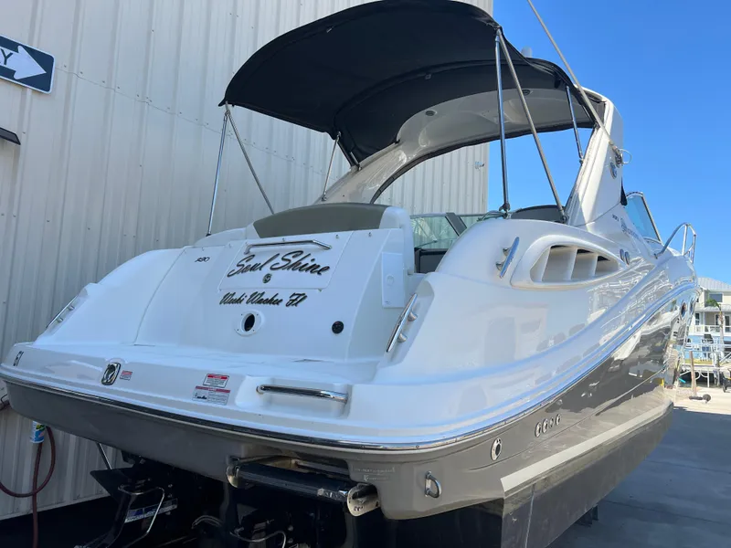 Slide: The Image of 2006 Sea Ray 290 Sundancer boat with black canopy, docked near a building. - 2