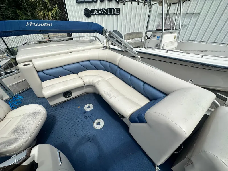 Slide: The Image of 2008 Manitou 24 Legacy boat interior with blue and white seating, docked near other boats. - 4