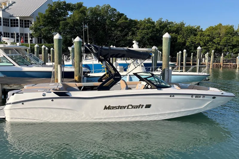 Slide: The Image of 2025 MasterCraft XT24 boat docked in marina, surrounded by water and trees. - 0