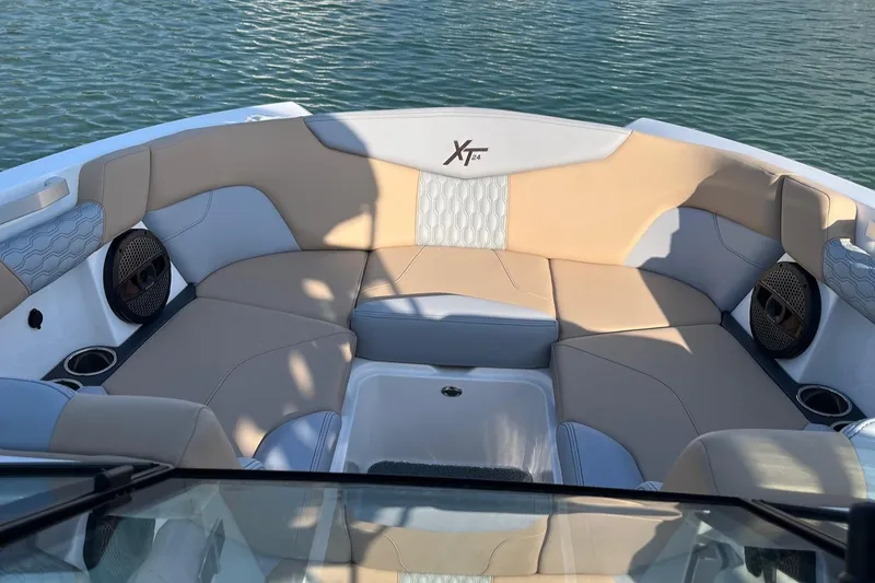 Slide: The Image of 2025 MasterCraft XT24 boat interior with beige and white seating, on calm water. - 2