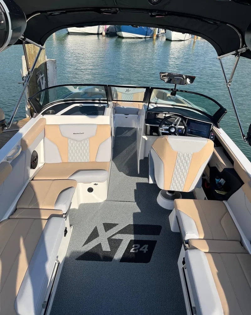 Slide: The Image of 2025 MasterCraft XT24 boat interior with beige seating, sleek design, and waterfront view. - 5