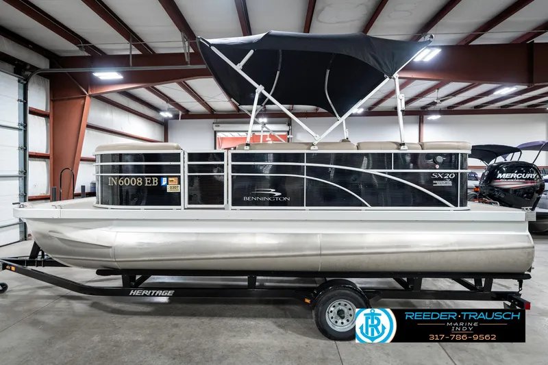Slide: The Image of 2018 Bennington 20 SLMX pontoon boat in showroom, black canopy, on trailer. - 11