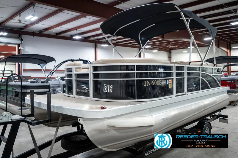Slide: The Image of 2018 Bennington 20 SLMX pontoon boat in showroom, featuring black canopy and sleek design. - 2
