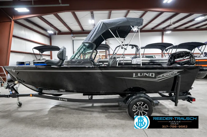 Slide: The Image of 2025 Lund 1775 Adventure Sport boat in showroom, featuring a sleek black design and Mercury engine. - 10
