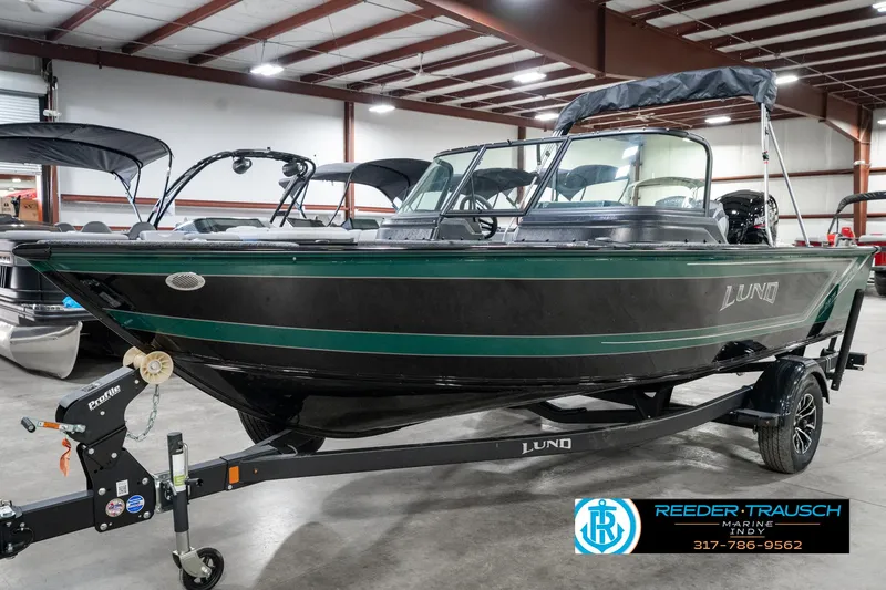 Slide: The Image of 2025 Lund 1875 Impact XS boat in showroom, black and green design, on trailer. - 2