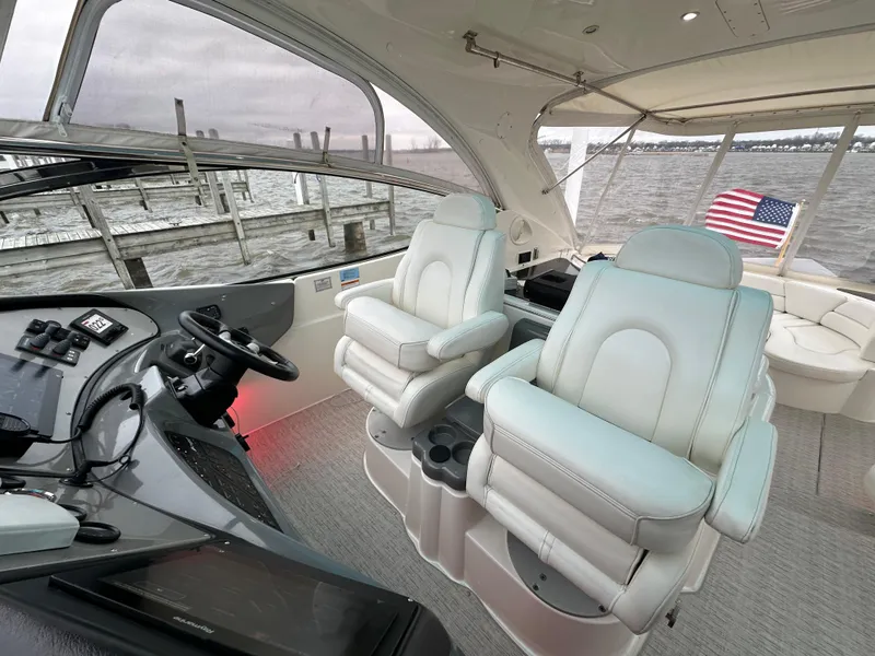 Slide: The Image of 2005 Cruisers Yachts 540 Express interior with helm, plush seating, and American flag. - 12