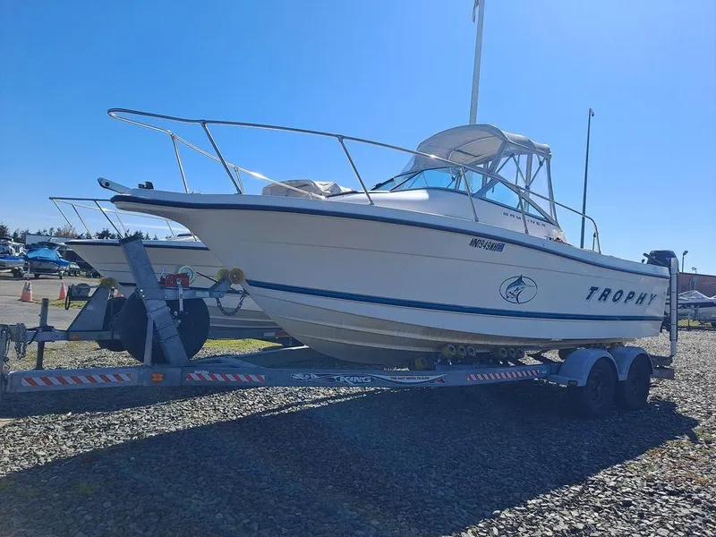Slide: The Image of 1998 Bayliner 2052 Trophy boat on trailer, parked on gravel under clear blue sky. - 0