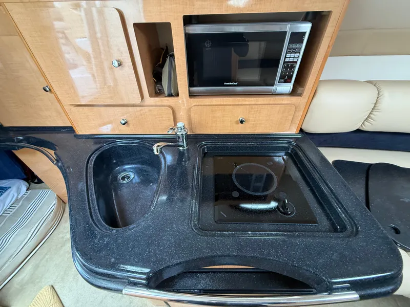 Slide: The Image of 2014 Glastron GS 289 boat interior with kitchenette, featuring sink, stove, and microwave. - 46