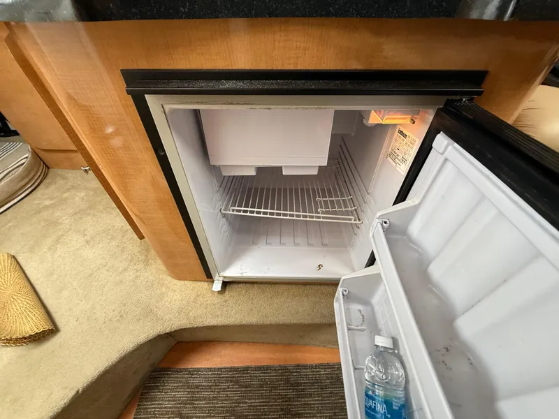 Slide: The Image of 2014 Glastron GS 289 boat interior with open mini fridge, showing shelves and a water bottle. - 49