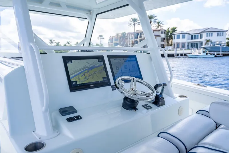 Slide: The Image of 2018 Yellowfin 42 boat dashboard with navigation screens and steering wheel, near waterfront homes. - 22