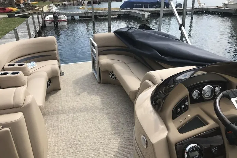 Slide: The Image of 2018 Bennington 23GSRFB pontoon boat interior with beige seating and dashboard, docked by the water. - 17