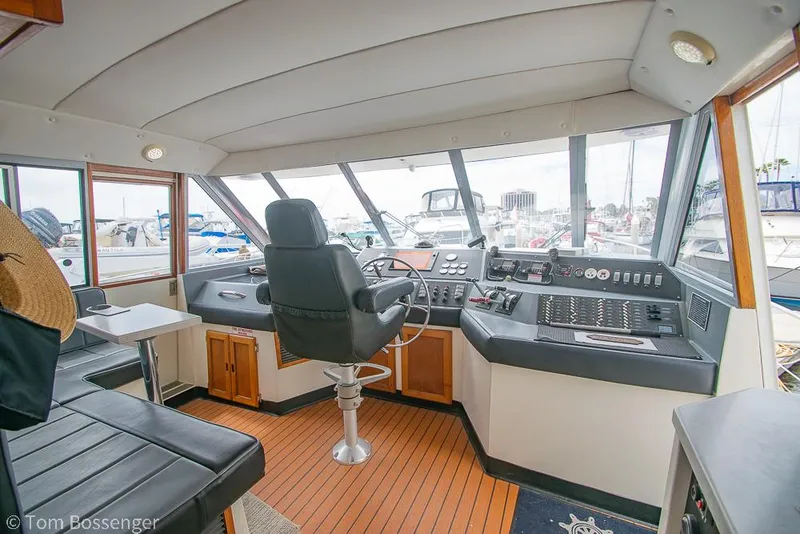 Slide: The Image of 1986 Bayliner 4588 Pilothouse interior with helm, seating, and panoramic windows at marina. - 31