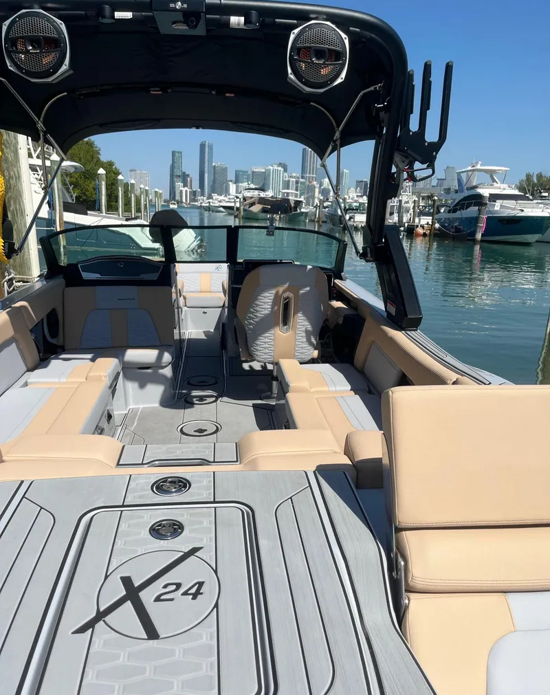 Slide: The Image of 2025 MasterCraft X24 boat with spacious seating, docked in a marina with city skyline. - 2