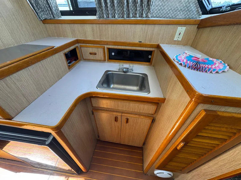 Slide: The Image of Compact kitchen area in a 1988 Bertram 28 Sport Fisherman boat, featuring a sink and wooden cabinetry. - 15