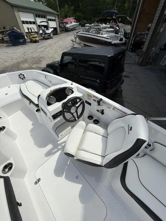 Slide: The Image of 2025 Stingray 182SC boat interior with white seating and steering wheel, parked near a garage. - 10
