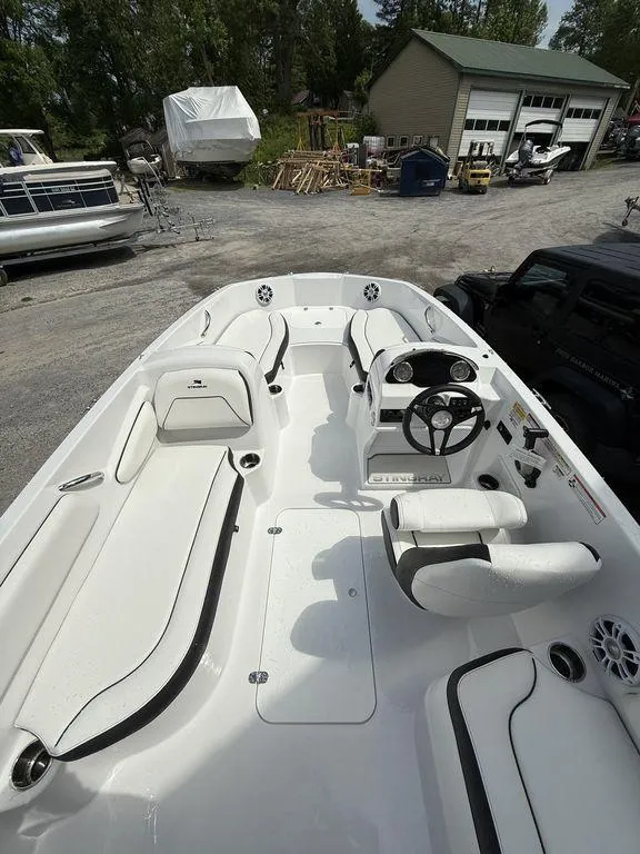 Slide: The Image of 2025 Stingray 182SC boat interior with white seating and steering wheel, parked outdoors. - 14