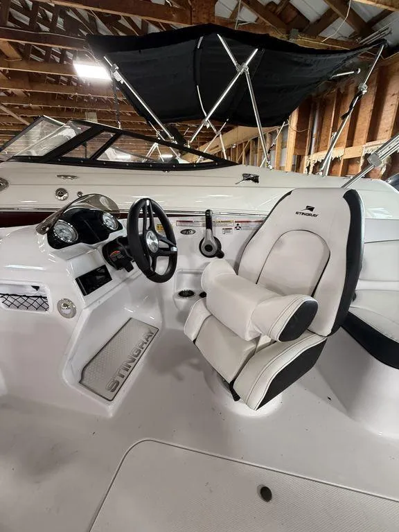 Slide: The Image of 2025 Stingray 182SC boat interior with white seating and steering wheel in a wooden boathouse. - 17