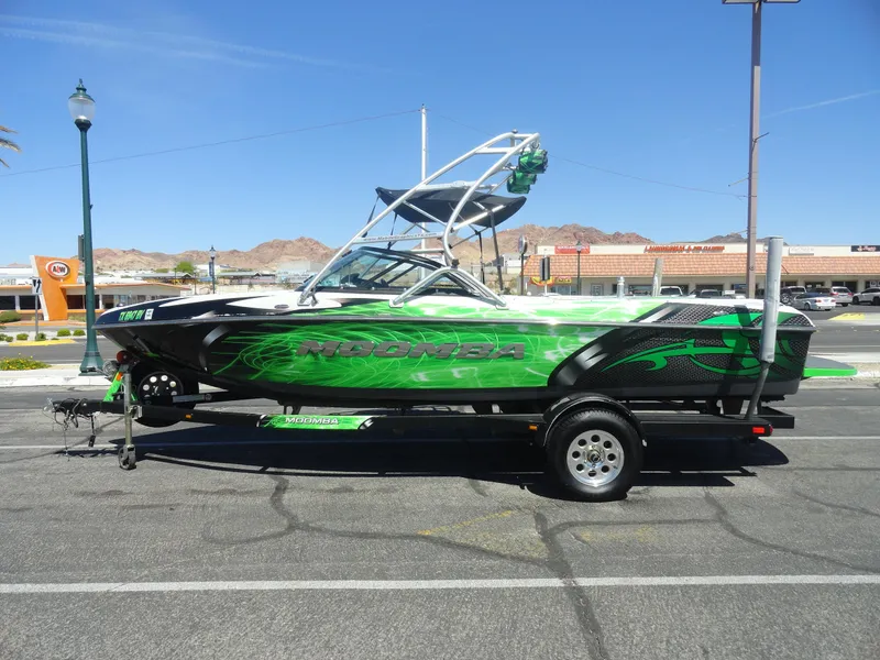 Slide: The Image of 2011 Moomba Outback V boat with vibrant green graphics on a trailer in a parking lot. - 1