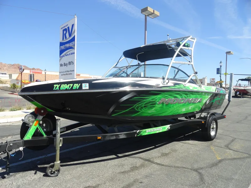 Slide: The Image of 2011 Moomba Outback V boat with green graphics on a trailer in a parking lot. - 2