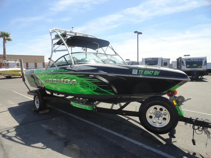 Slide: The Image of 2011 Moomba Outback V boat with green graphics on a trailer in a parking lot. - 4