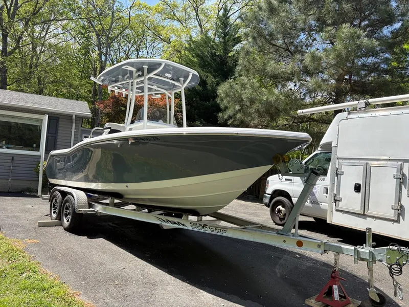 Slide: The Image of 2023 Tidewater 210 CC Adventure boat on trailer, parked outdoors near trees and vehicles. - 3